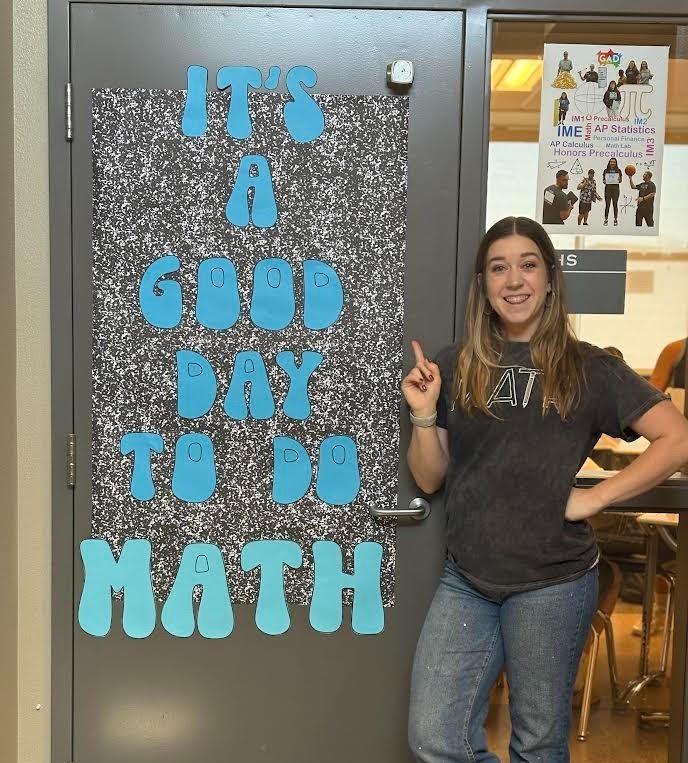Mrs. Gonzalez standing outside her math room with its amazing poster