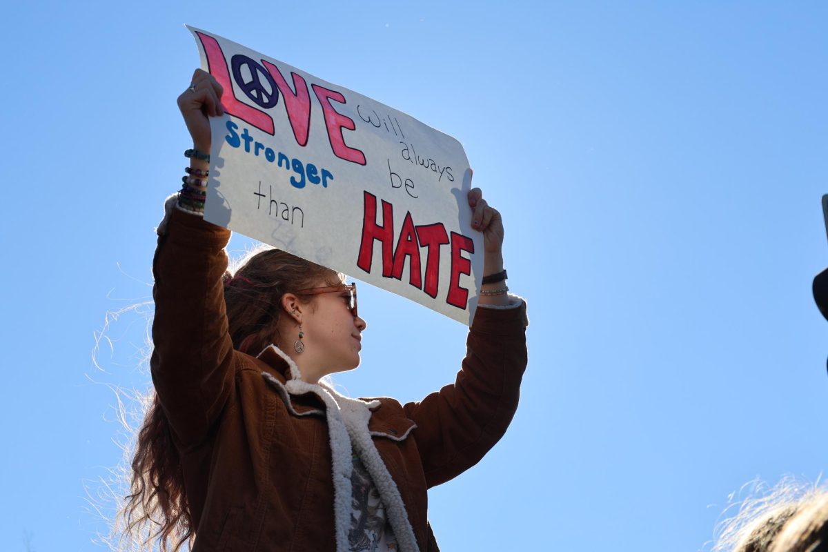 A student holds up her poster, reading "Love will always be stronger than hate."